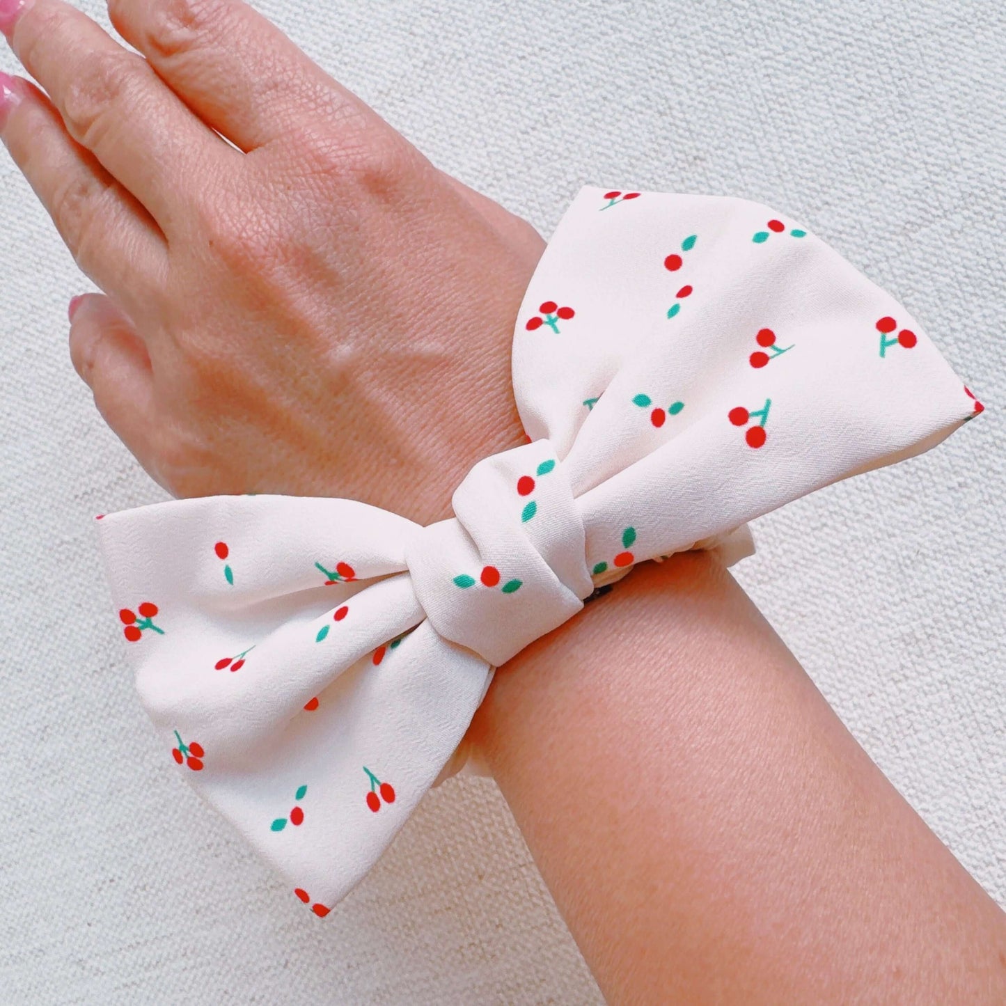 Cherry Lovely Bow Tie Hair Scrunch featuring a cherry print design and a cute bow tie on a wrist.