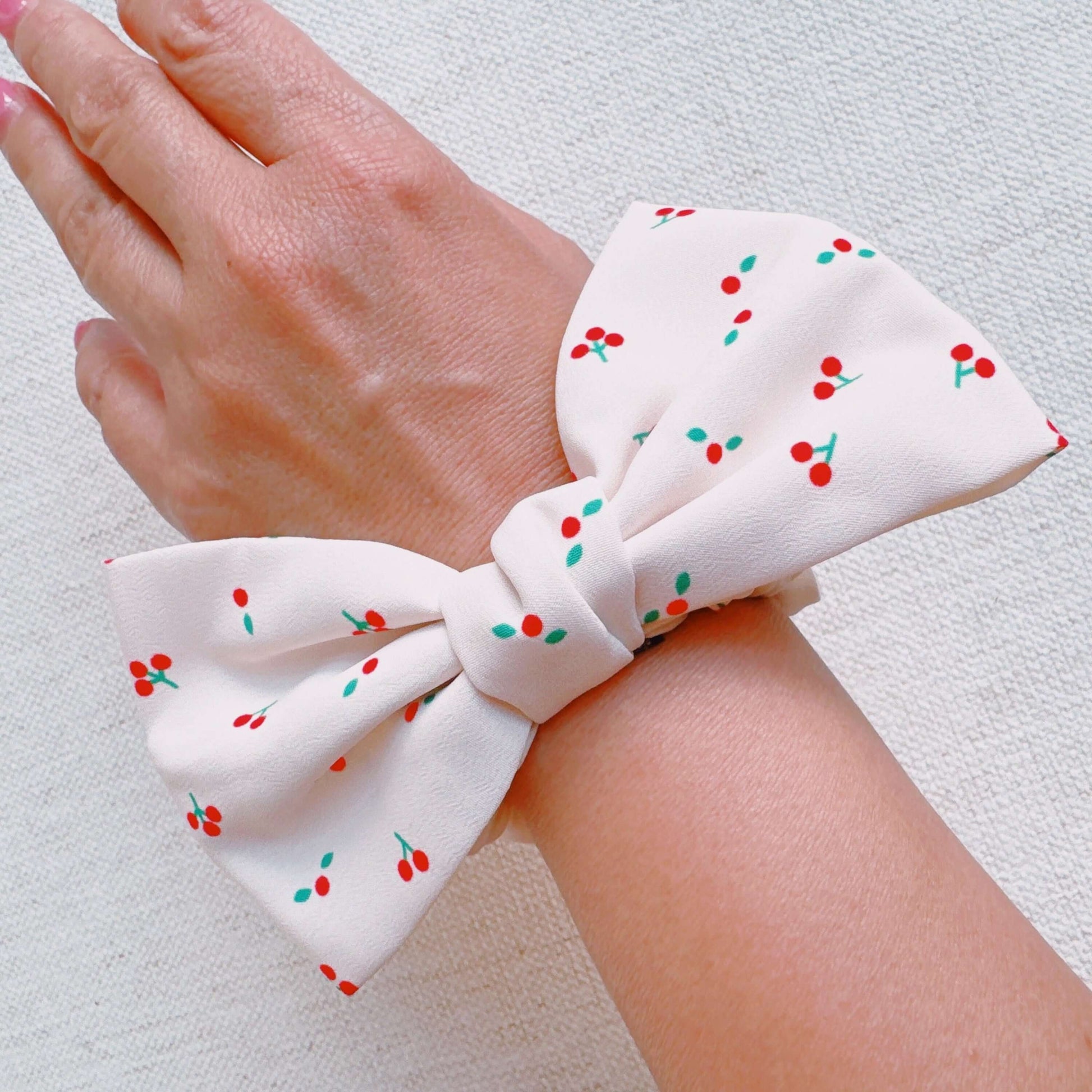Cherry Lovely Bow Tie Hair Scrunch featuring a cherry print design and a cute bow tie on a wrist.